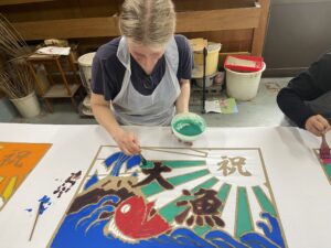 a woman painting a Tairyo-bata fishing boat flag with red, blue and green paint