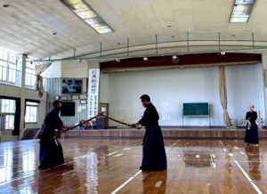 Kendo class in a hall. Two men in robes are Japanese fencing.