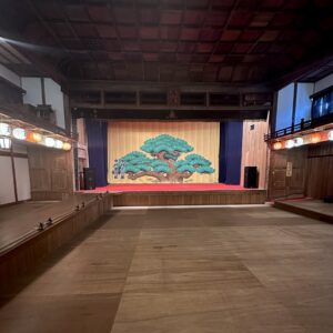 Joge theatre with a stage and screen with a tree on at the back of the room