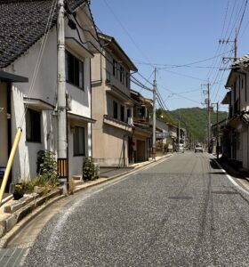 A quiet Joge street. Tarmac road, older buildings and a blue sky