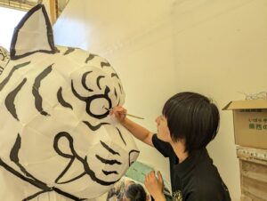 Lady painting a tiger nebuta float, currently black and white
