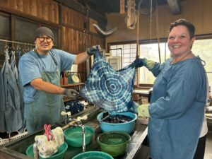 Ali wearing a blue overall holding up her indigo design with Mr. Kawasaki